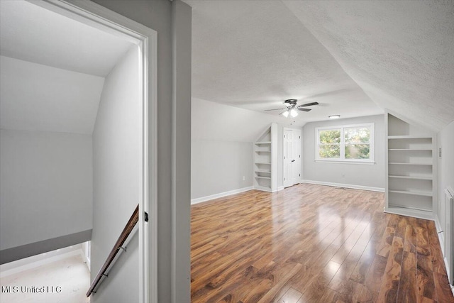 additional living space featuring hardwood / wood-style floors, ceiling fan, a textured ceiling, vaulted ceiling, and built in shelves