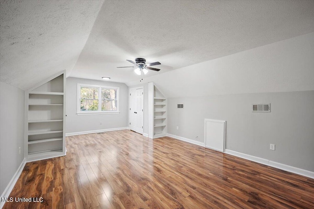 bonus room featuring lofted ceiling, a textured ceiling, wood-type flooring, and built in shelves