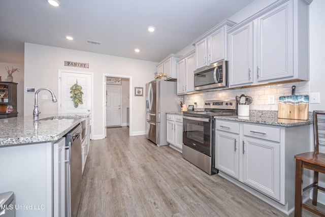 kitchen with light stone countertops, sink, stainless steel appliances, tasteful backsplash, and light hardwood / wood-style flooring