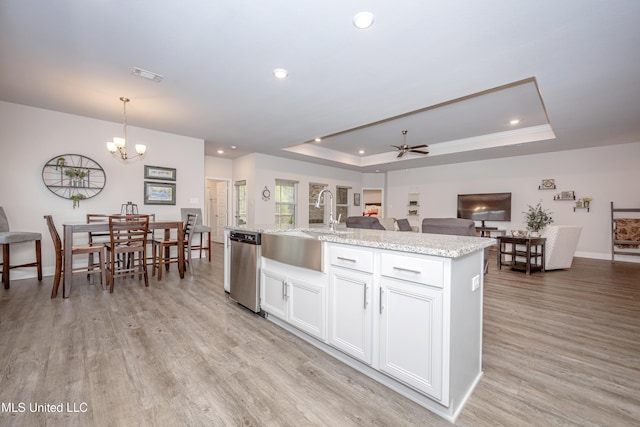 kitchen with stainless steel dishwasher, a tray ceiling, a kitchen island with sink, white cabinetry, and hanging light fixtures