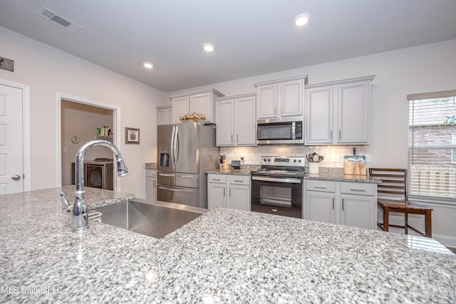 kitchen with light stone countertops, appliances with stainless steel finishes, backsplash, and sink