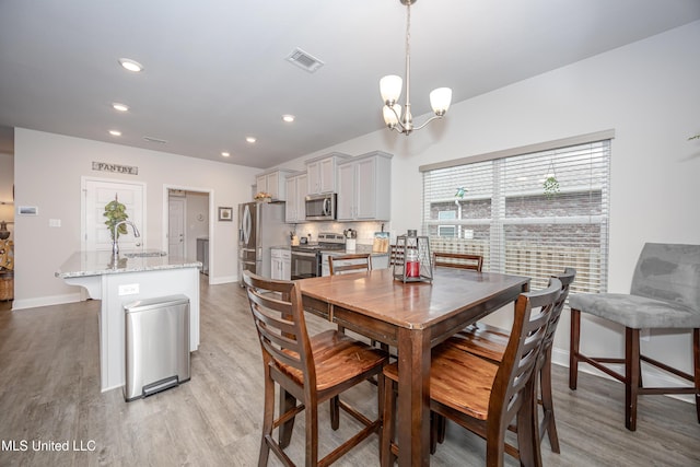 dining space with sink, a chandelier, and light wood-type flooring