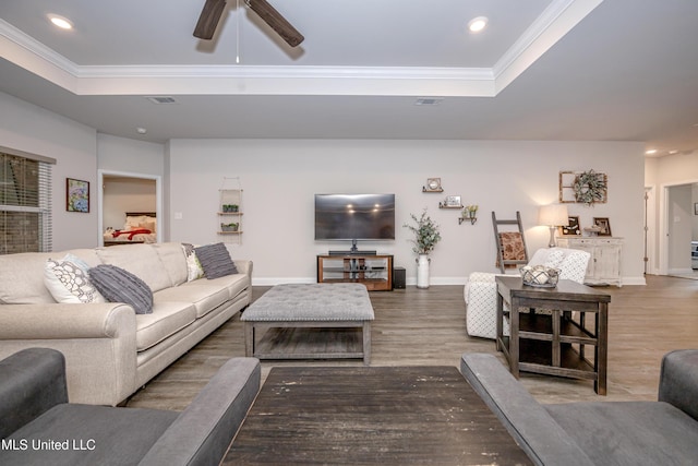 living room with hardwood / wood-style floors, ceiling fan, ornamental molding, and a tray ceiling