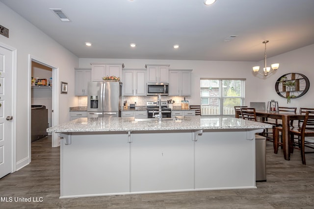 kitchen featuring a kitchen island with sink, a breakfast bar, light stone counters, and appliances with stainless steel finishes