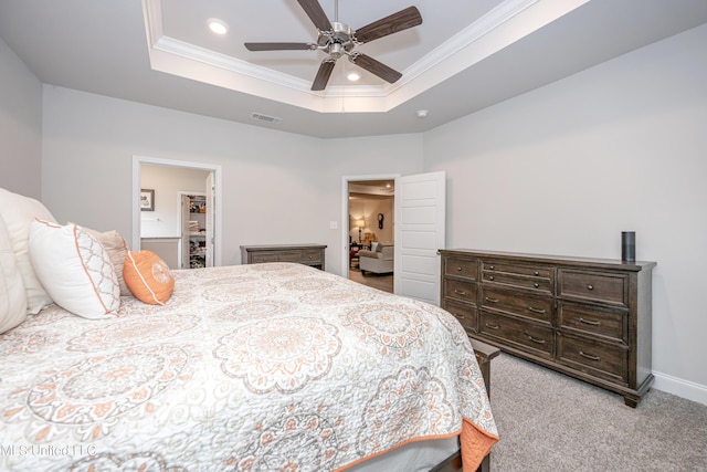 bedroom featuring light carpet, ornamental molding, a tray ceiling, ceiling fan, and connected bathroom