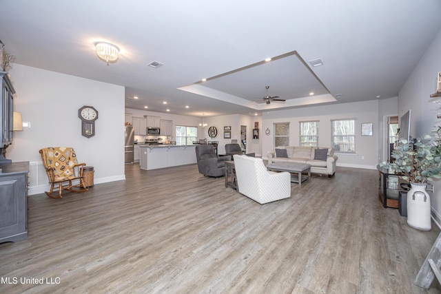 living room with a raised ceiling, ceiling fan, and light wood-type flooring