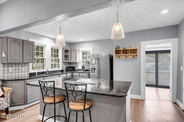 kitchen featuring black microwave, gray cabinetry, backsplash, stainless steel fridge with ice dispenser, and stovetop