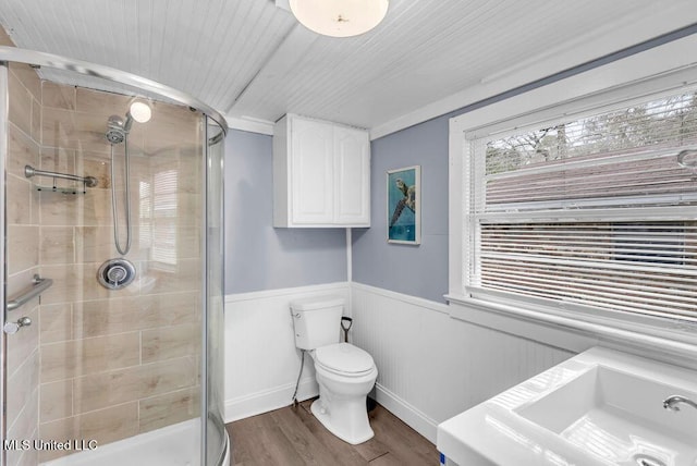 bathroom with toilet, a wainscoted wall, wood finished floors, and a stall shower