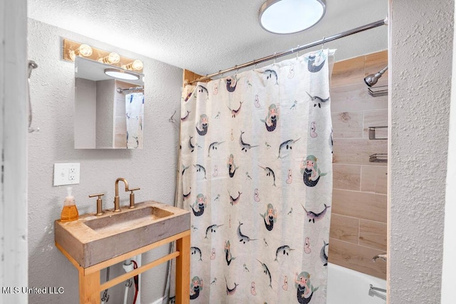 full bathroom featuring a sink, shower / bath combination with curtain, a textured ceiling, and a textured wall