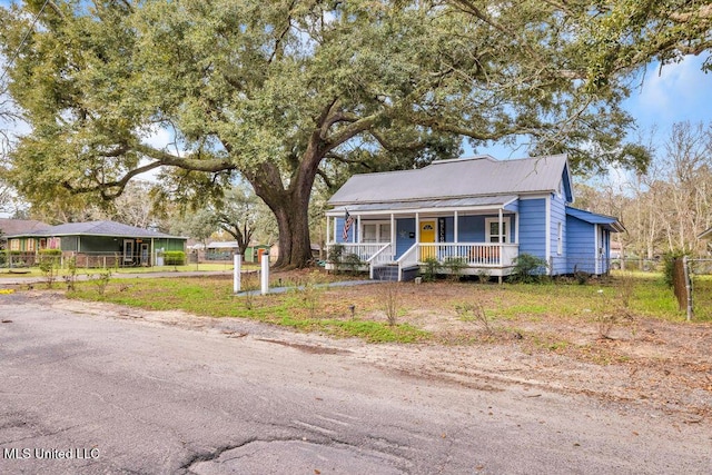 bungalow-style home with covered porch, fence, and metal roof