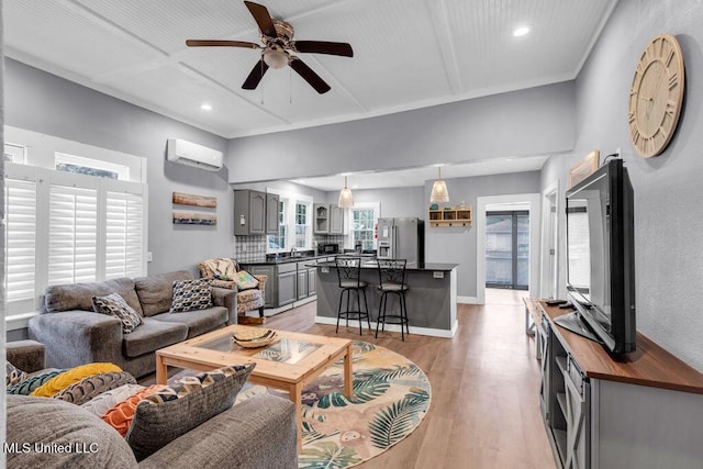 living room featuring baseboards, light wood-style flooring, ceiling fan, a wall mounted air conditioner, and recessed lighting