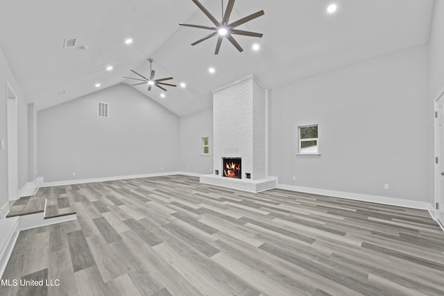 unfurnished living room with ceiling fan, light hardwood / wood-style floors, high vaulted ceiling, and a brick fireplace