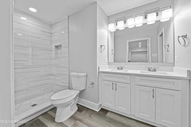 bathroom with hardwood / wood-style floors, vanity, a tile shower, and toilet