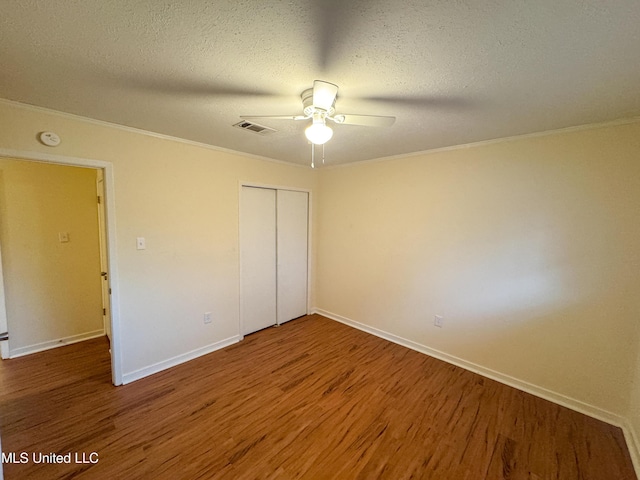 unfurnished bedroom with baseboards, wood finished floors, a textured ceiling, crown molding, and a closet