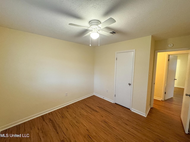 unfurnished room featuring visible vents, ceiling fan, a textured ceiling, wood finished floors, and baseboards