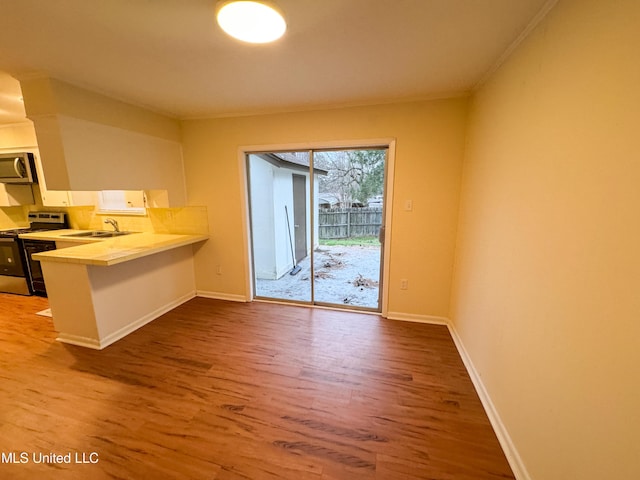 kitchen featuring stainless steel appliances, light countertops, wood finished floors, a peninsula, and baseboards