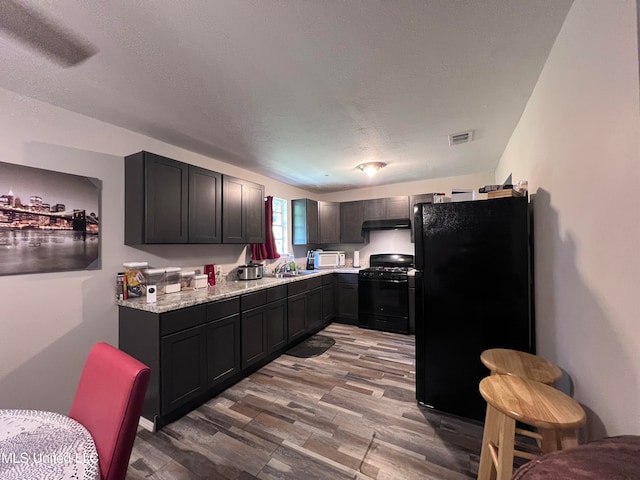 kitchen featuring light stone counters, a textured ceiling, light hardwood / wood-style flooring, black appliances, and sink