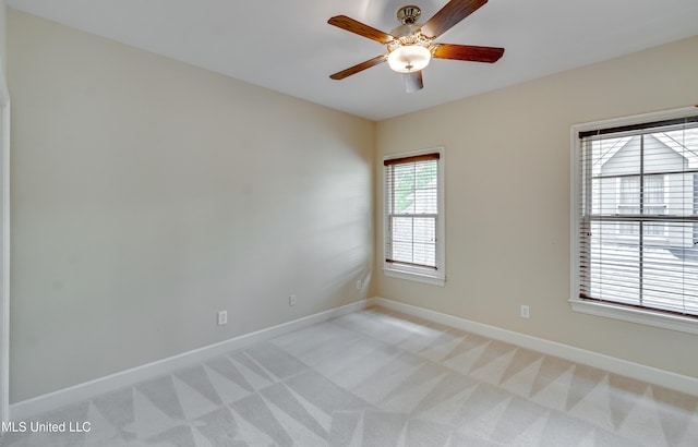 spare room featuring light colored carpet, baseboards, and a ceiling fan