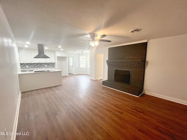 unfurnished living room with hardwood / wood-style flooring, ceiling fan, crown molding, and a fireplace