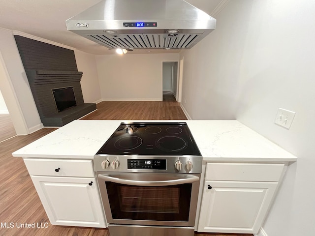 kitchen with wall chimney range hood, light hardwood / wood-style floors, a fireplace, white cabinets, and high end stainless steel range