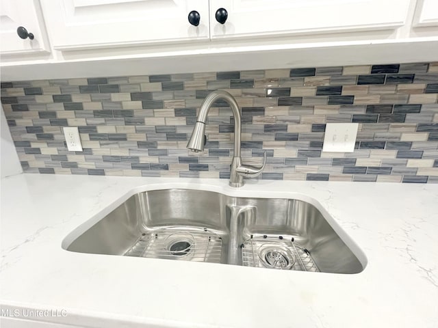 interior details with white cabinets, backsplash, light stone countertops, and sink