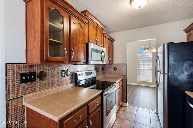 kitchen with stainless steel appliances, light tile patterned floors, a textured ceiling, and backsplash