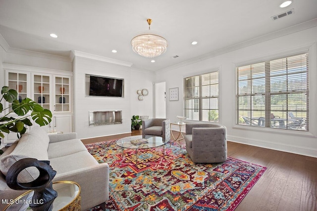 living room with ornamental molding, a chandelier, dark hardwood / wood-style floors, and a large fireplace