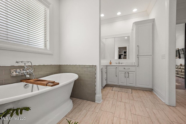 bathroom featuring tile walls, vanity, crown molding, and a bathtub