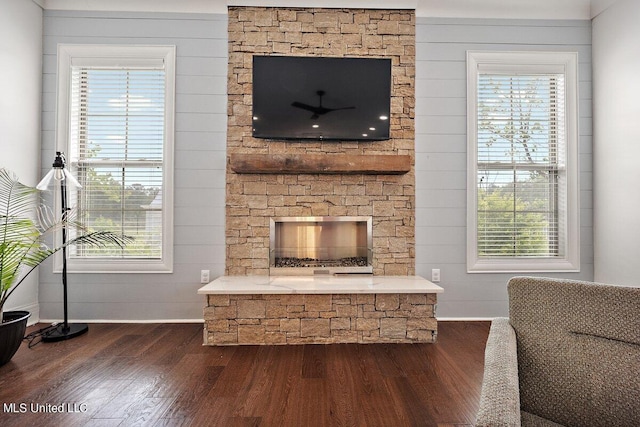 living room featuring wooden walls, a stone fireplace, and dark hardwood / wood-style floors