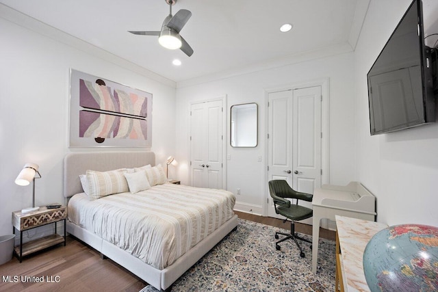 bedroom featuring crown molding, two closets, dark hardwood / wood-style floors, and ceiling fan