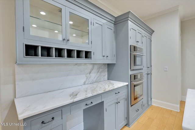 kitchen with light stone counters, light hardwood / wood-style floors, decorative backsplash, stainless steel double oven, and crown molding