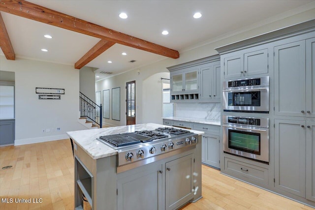 kitchen featuring gray cabinets, appliances with stainless steel finishes, a center island, beam ceiling, and backsplash