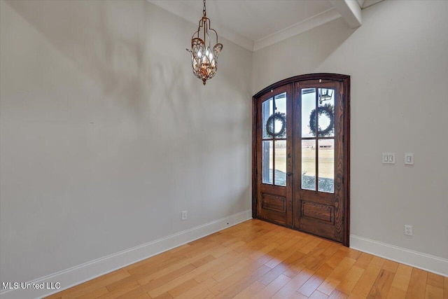 foyer entrance with french doors, crown molding, light hardwood / wood-style floors, and a notable chandelier