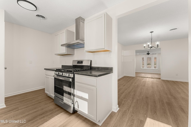 kitchen featuring stainless steel range with gas cooktop, white cabinets, wall chimney range hood, pendant lighting, and light hardwood / wood-style flooring