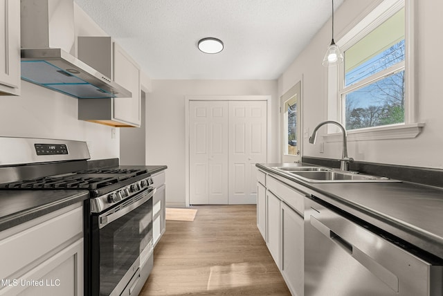 kitchen with decorative light fixtures, wall chimney range hood, sink, appliances with stainless steel finishes, and white cabinets