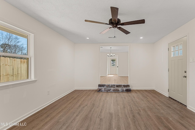 unfurnished living room with ceiling fan with notable chandelier, wood-type flooring, a textured ceiling, and a healthy amount of sunlight