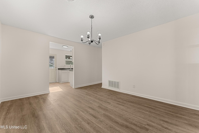 unfurnished dining area featuring hardwood / wood-style floors, a textured ceiling, and a chandelier