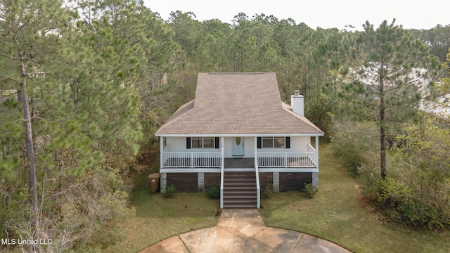 view of front facade with a view of trees, a chimney, roof with shingles, covered porch, and stairs