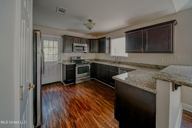 kitchen featuring dark brown cabinetry, stainless steel appliances, a sink, visible vents, and dark wood finished floors