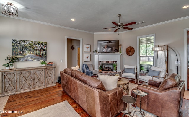 living room featuring hardwood / wood-style floors, crown molding, a fireplace, and ceiling fan with notable chandelier