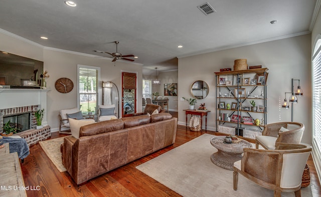 living room with ornamental molding, a brick fireplace, wood-type flooring, and ceiling fan