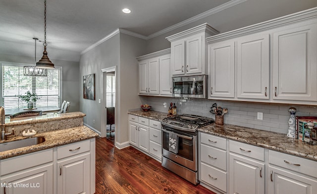 kitchen with appliances with stainless steel finishes, white cabinetry, pendant lighting, ornamental molding, and dark hardwood / wood-style floors