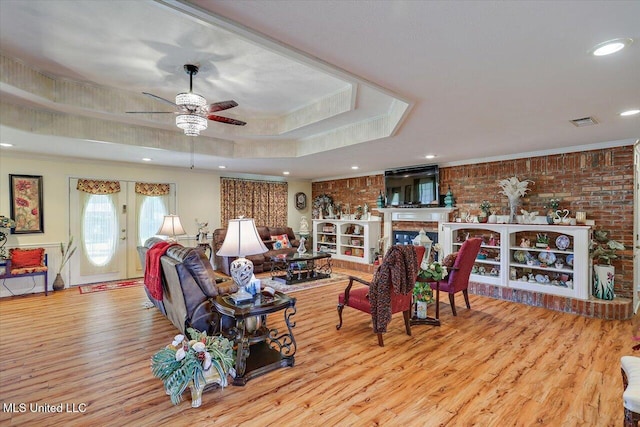 living room with visible vents, crown molding, wood finished floors, ceiling fan, and a raised ceiling