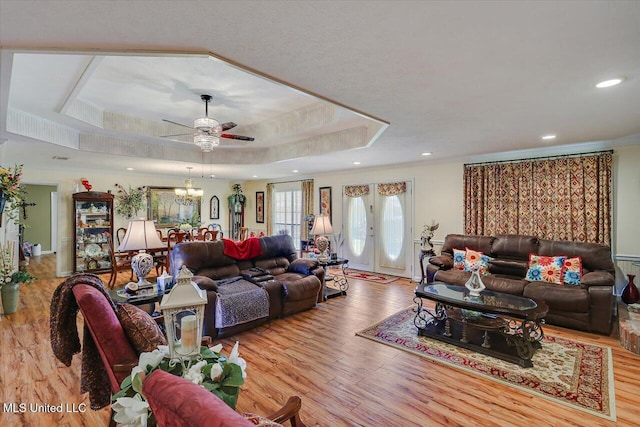 living area with crown molding, wood finished floors, recessed lighting, a raised ceiling, and ceiling fan with notable chandelier
