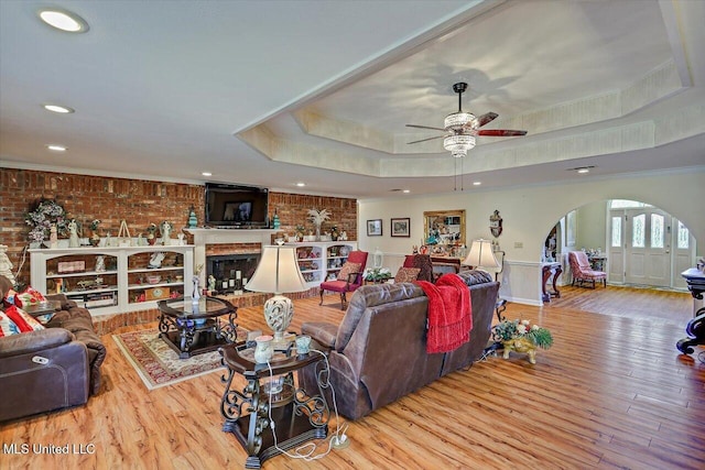 living area featuring recessed lighting, arched walkways, a raised ceiling, and wood finished floors