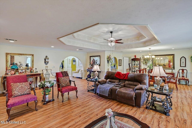 living area with a healthy amount of sunlight, a raised ceiling, ceiling fan with notable chandelier, and light wood-type flooring