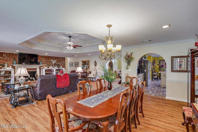 dining room with visible vents, light wood-style floors, a wainscoted wall, arched walkways, and ceiling fan with notable chandelier