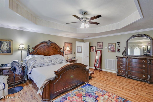 bedroom featuring crown molding, a tray ceiling, visible vents, and wood finished floors