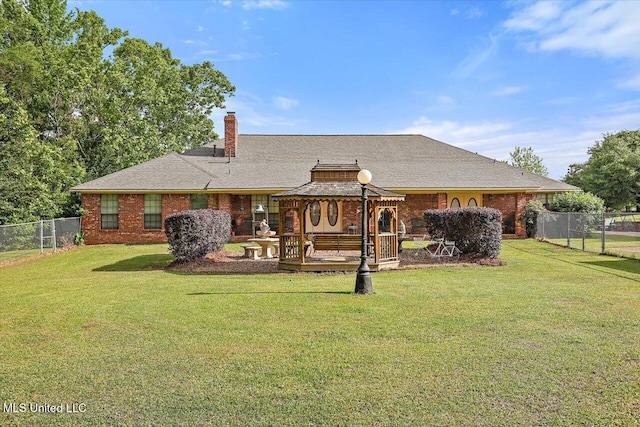 back of house with a lawn, fence, a chimney, brick siding, and a gazebo