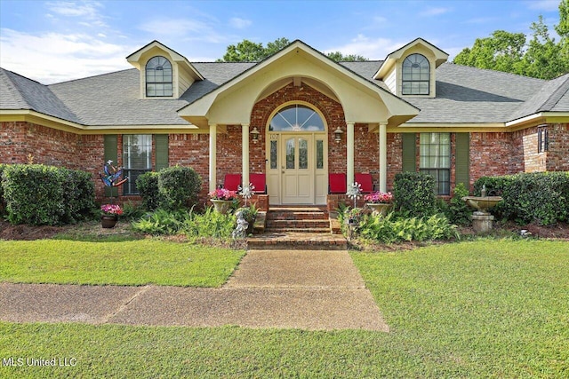 view of front of property featuring a shingled roof, a front lawn, and brick siding